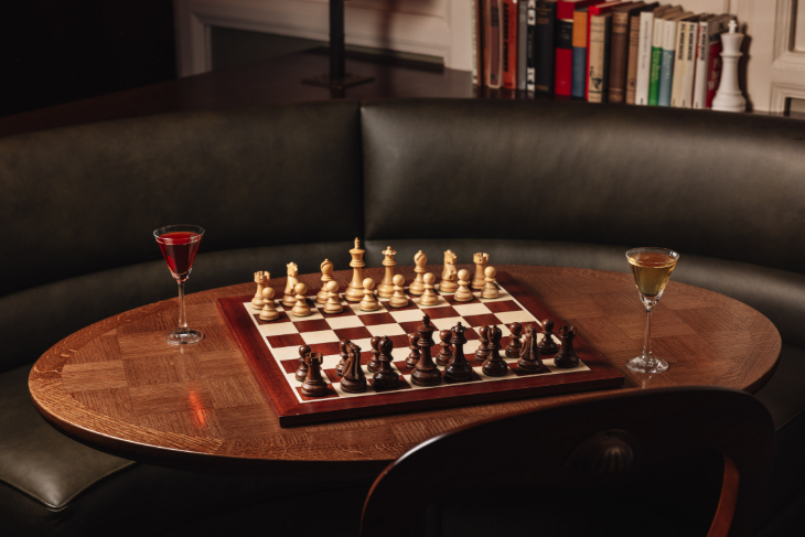 A wooden table with a chess board and two glasses of drink