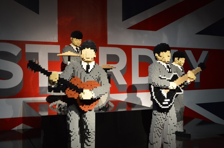 Life-sized Lego sculptures of The Beatles performing on a stage in front of a Union Jack backdrop with the word "YESTERDAY" in large letters.