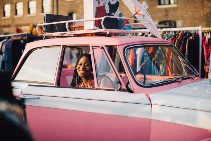 Things to do in London today: a woman sitting in a pink classic car in front of racks of clothing