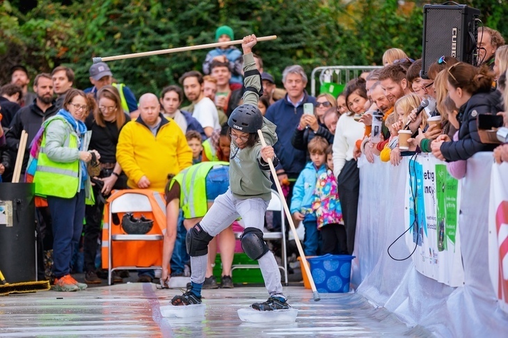 Things to do in London today: a person holding wooden poles with ice blocks strapped to their shoes skiiing in front of a crowd