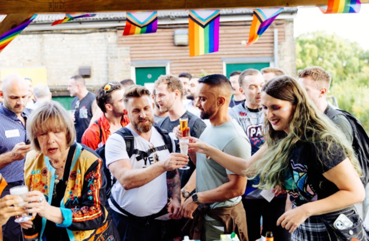 Things to do in London this weekend: people gathered around a bar or stall, some holding beers, beneath LGBTQ+ flags