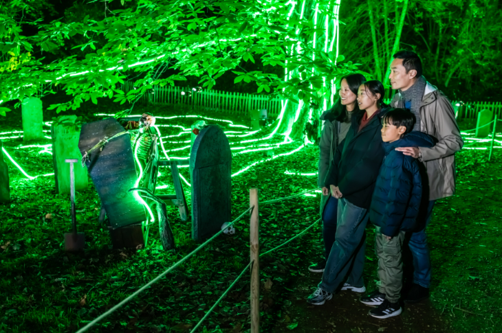 A family viewing a graveyard set up beneath green illuminated trees