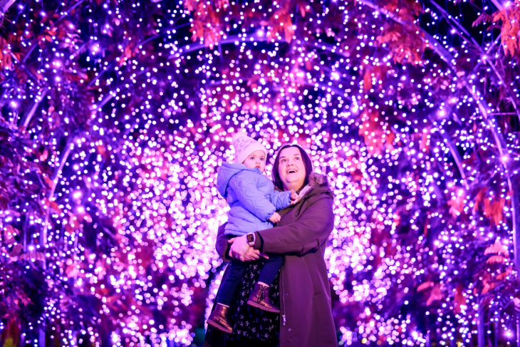Winter light trails festivals near London Christmas 2026: a woman holding a child in a tunnel made of pink fairy lights