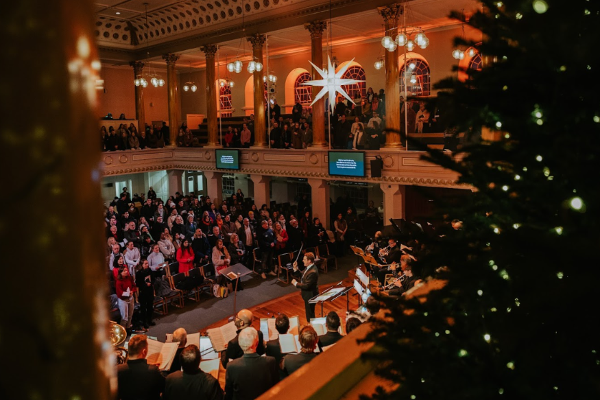 Christmas carol concerts London 2026: the interior of a church decorated for Christmas, with a conductor leading a choir