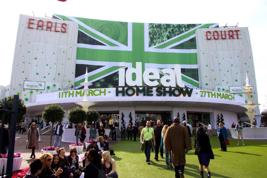 A large crowd gathers outside the Earls Court Exhibition Centre in London for the Ideal Home Show. The building is draped in a green and white Union Jack banner with the event name and dates, March 11th to 27th, displayed across the front.
