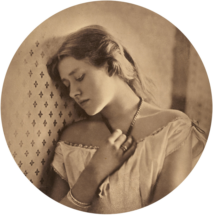 A sepia-toned circular portrait of a young woman with long, light-colored hair, leaning her head against a patterned wall. She wears an off-the-shoulder white dress and holds a dark necklace with her hand, looking downward with a pensive expression.
