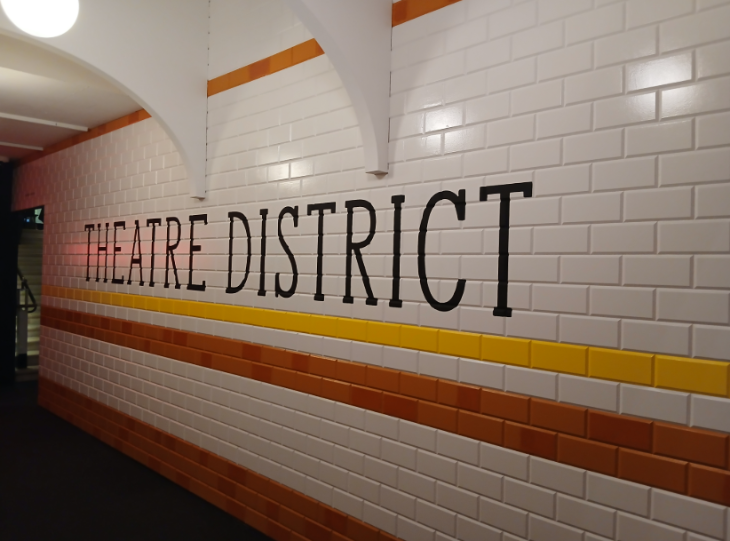 A Tube station style tiled wall with 'Theatre District' written on it