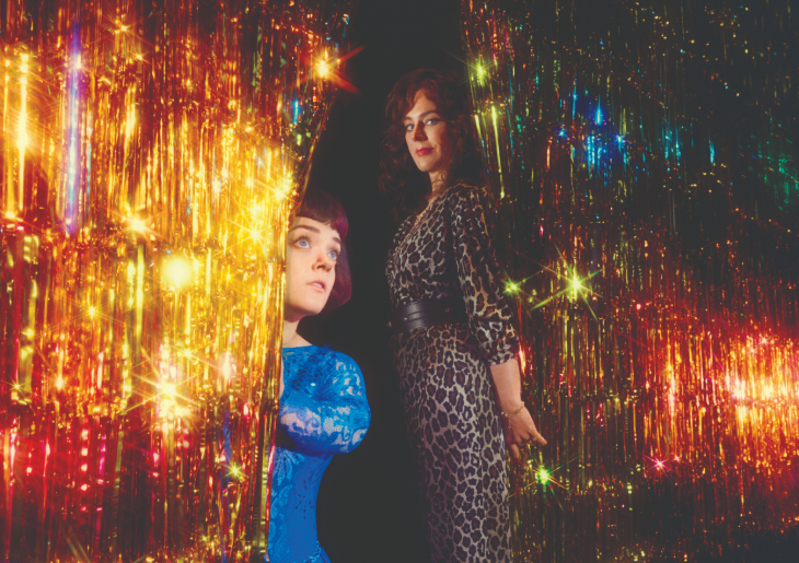 Things to do in London in December 2026: Francesca Mills and Jill Halfpenny peeking out from behind a tinsel curtain