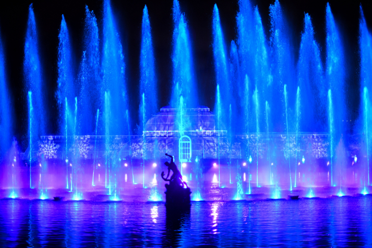 Things to do in London in November 2026: illuminated blue fountains in front of the Palm House at Kew