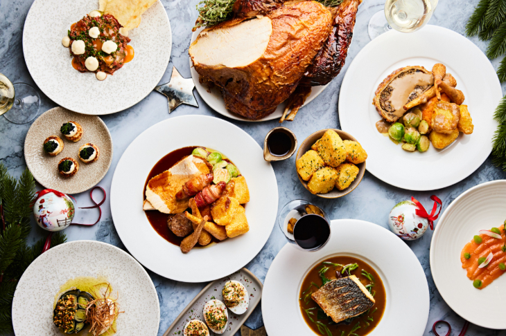Where to book dinner on Christmas Day 2026 in London: a flatlay view of several plates on the table for Christmas dinner, with dishes including roast turkey, roast potatoes, parsnips and pigs in blankets