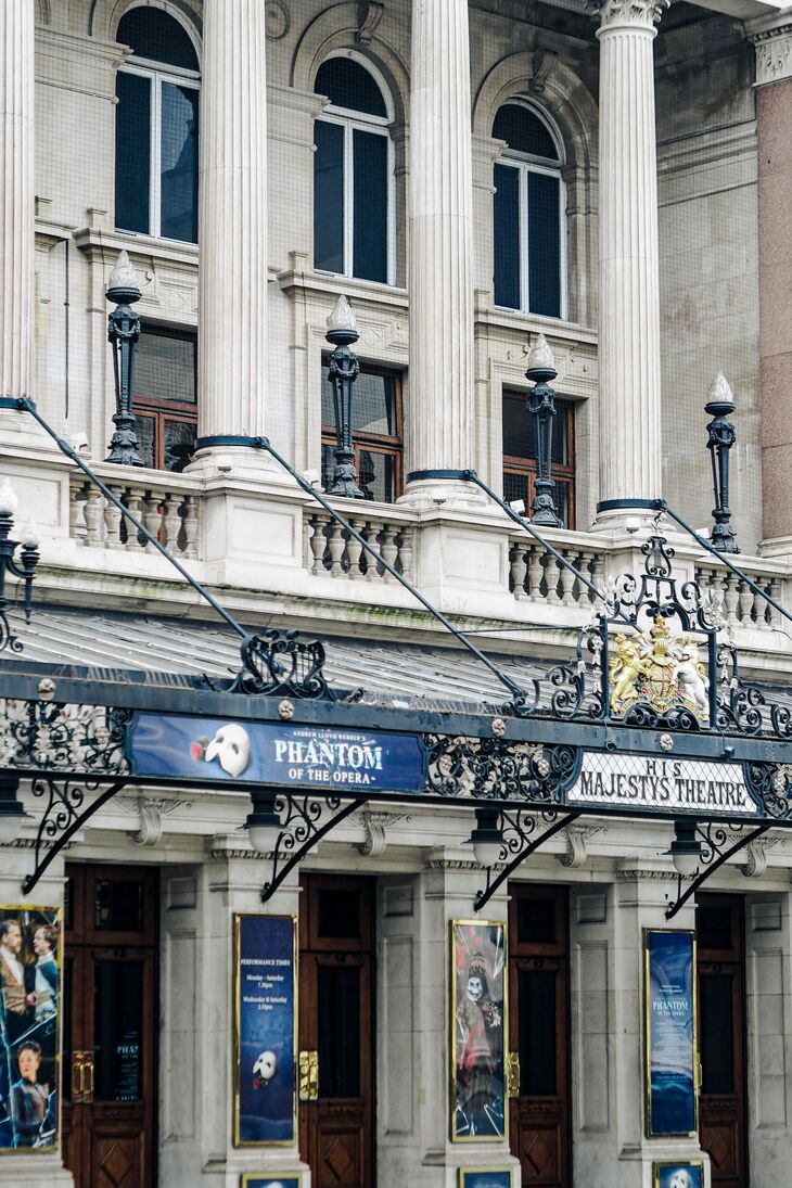 The ornate facade of His Majesty's Theatre in London, featuring white columns, arched windows, and a black wrought-iron marquee advertising 