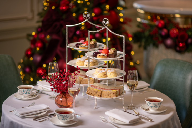 Best Christmas afternoon tea in London 2026:  two tiered afternoon tea stands side by side on a table, with a twinkling Christmas tree in the background