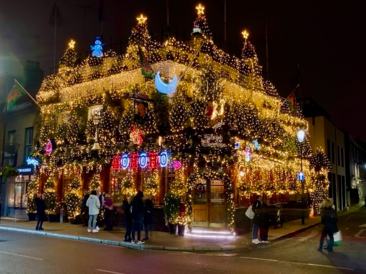 London Christmas light switch-ons 2026: the exterior of the Churchill Arms pub at night, covered in lights and Christmas trees