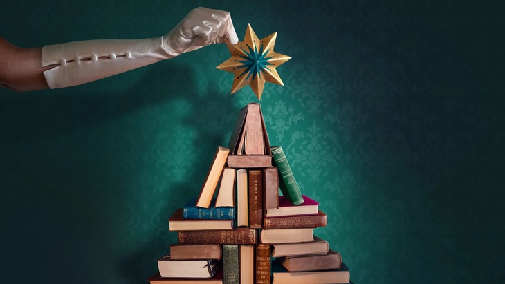 A star being placed on top of a book Christmas tree