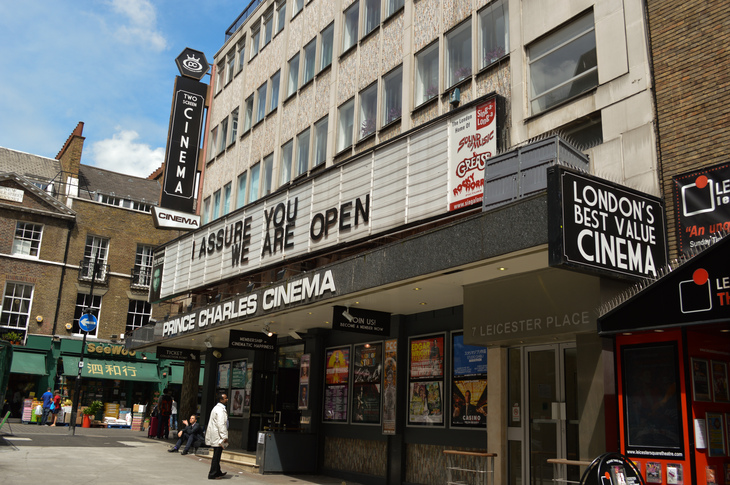 The Prince Charles Cinema in London, featuring a marquee that reads "I ASSURE YOU WE ARE OPEN" and posters for various films.