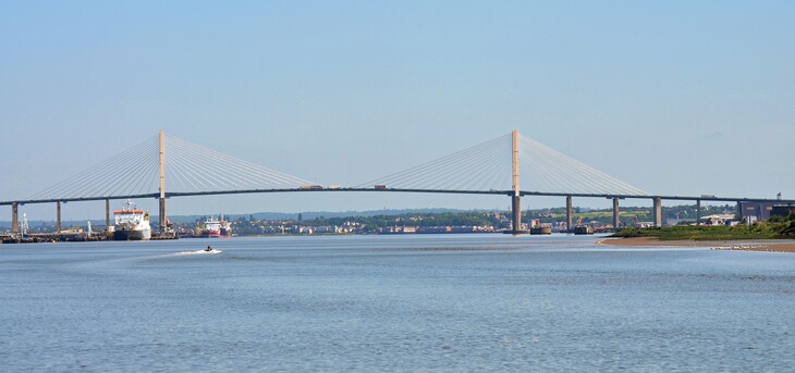 A wide shot of the Queen Elizabeth II Bridge, a cable-stayed bridge spanning the River Thames, under a clear blue sky.
