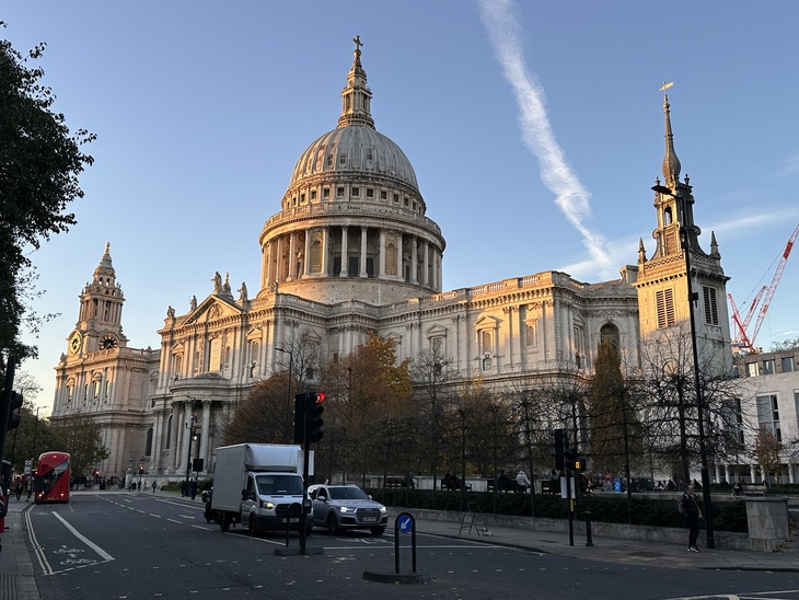 Things to do in London on Christmas Day 2026. St. Paul's Cathedral in London at sunset, viewed from a street with a red double-decker bus and white vehicles in the foreground.