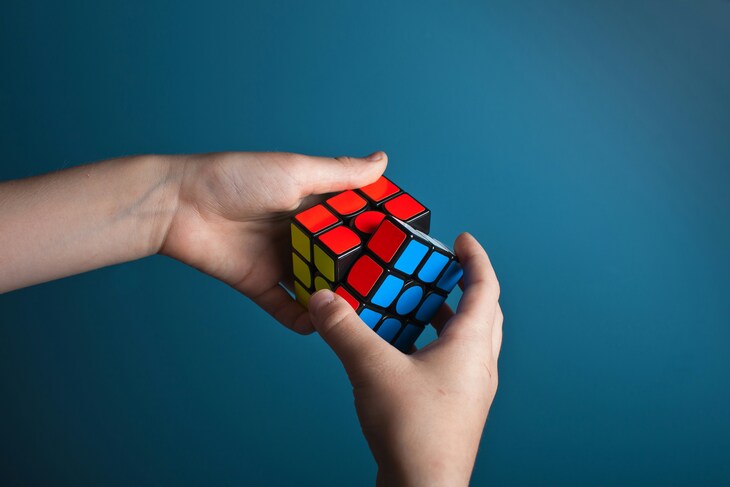 Things to do in London this weekend:  A person's hands holding and twisting a partially solved Rubik's cube against a solid blue background.