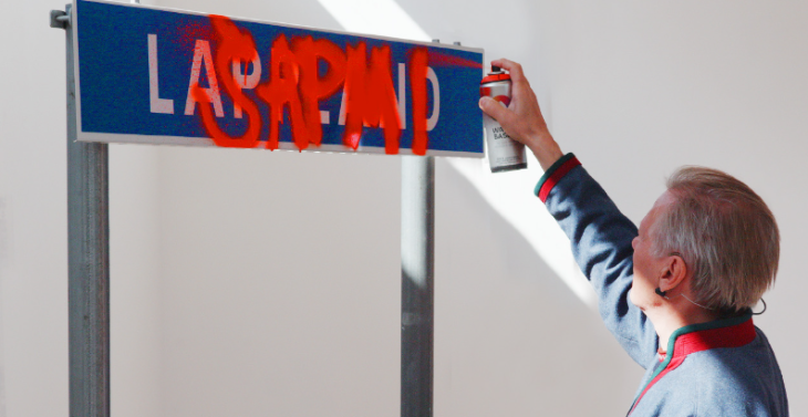 Things to do in London today: a person spray painting "SÁPMI" over a road sign which says "Lapland"