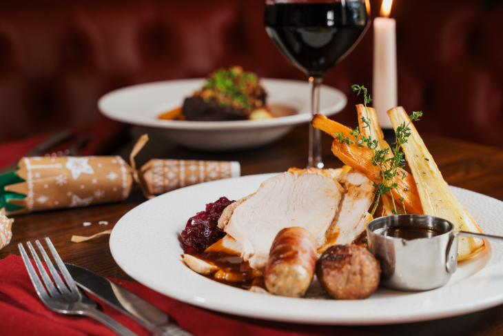 Which restaurants open in London on Christmas Day 2026: a plate of traditional Christmas dinner on a table along with a cracker, a glass of red wine, and a lit candle