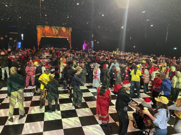 Christmas 2026 volunteering in London: A huge ballroom with chequerboard floors and twinkly lights overhead, packed with people