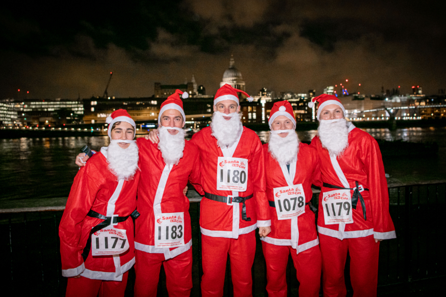 Things to do in London in December 2026: five people dressed as Santa posing for a photo beside the Thames at night