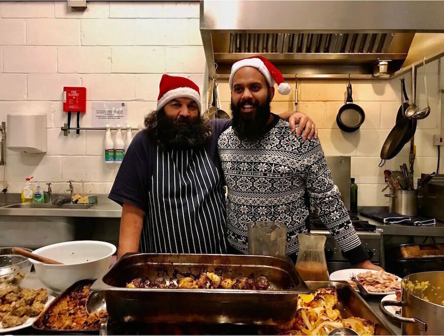 Christmas 2026 volunteering in London: two people wearing Santa hats and cooking aprons, standing in a kitchen with arms around each other 